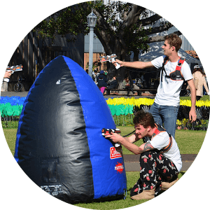 Two adult males use inflatable bunkers for cover at a University O Week activity